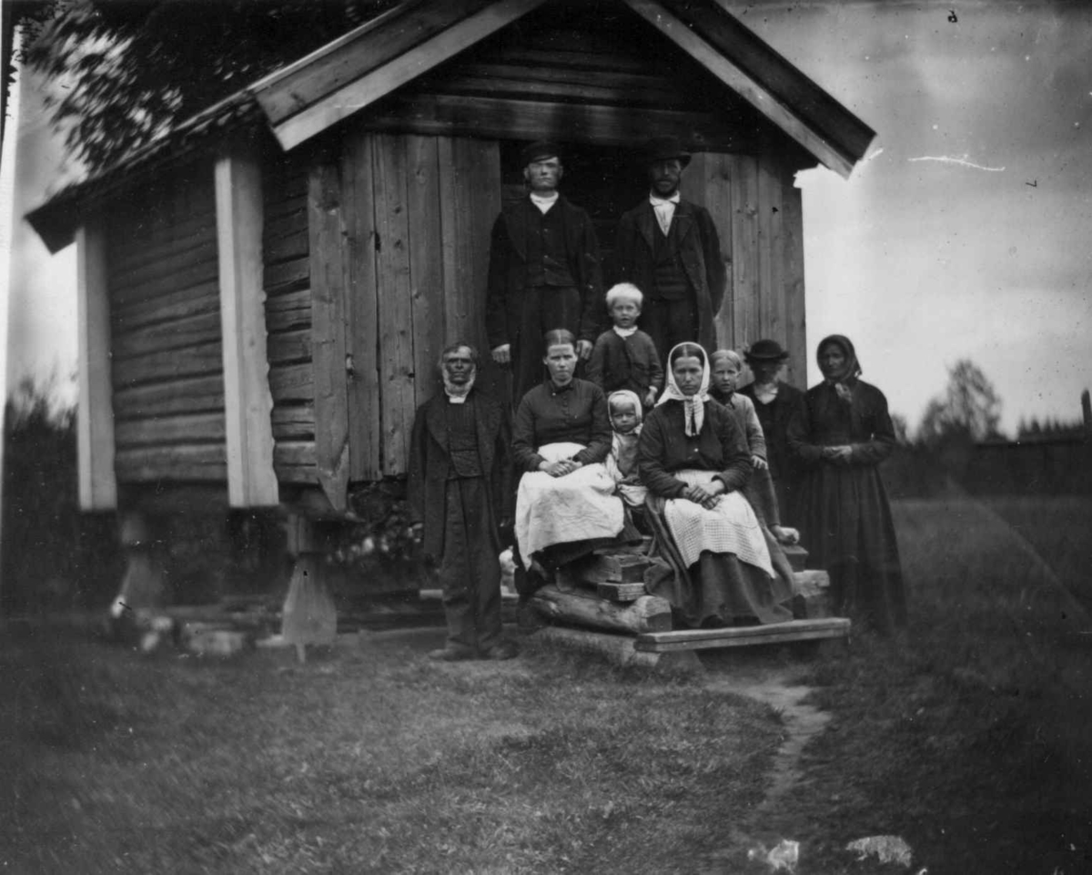 Fredrik Emil Faye, Arbeidsfolk, Dal gård, Ullensaker. Gruppe poserer på trapp foran uthus. Fra portrettserie av personer som bodde på eller besøkte Dal gård, Ullensaker, fotografert av gårdens eier, kammerherre Fredrik Emil Faye (1844-1903) i årene 1875-1900.