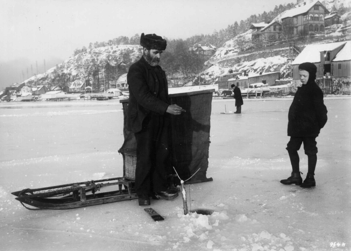 Hermann Christian Neupert, Vintermotiv. ant. 1908-1910.To fiskere på isen. Kjelke. Barn. Bebyggelse i bakgrunnen.
