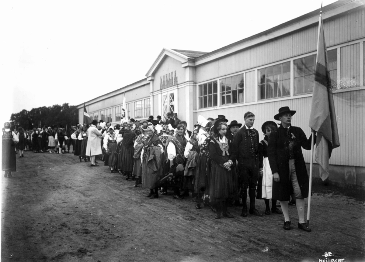 Hermann Christian Neupert, Nordisk Folkedansstevne - Oslo. 1925. Opptog av ant. finske folkedansere. Flagg. Norges Varemesse i bakgrunnen.