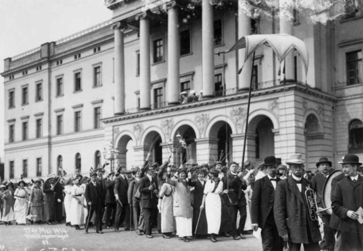 Hermann Christian Neupert, Oslo. Russ i 17. mai-tog 1914 foran Slottet. Festkledde i lange kjoler og dress. De kongelige ses på Slottsbalkongen.