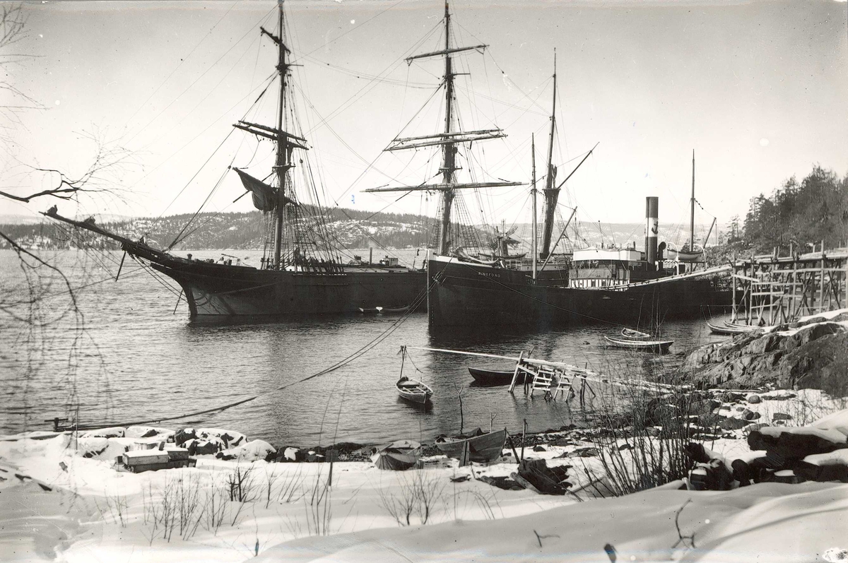 Axel Quinsgaard Wiborg, Islasting, Sønderstøen, Nesodden, Akershus, 1907. Seil- og dampskip, D/S "Ringfond", ved land med reisverk i tre med renne for lasting av isblokker fra land. Småbåter i forgrunnen. Fra serie tatt av iseksportør Axel Quinsgaard Wiborg (d. 1944).