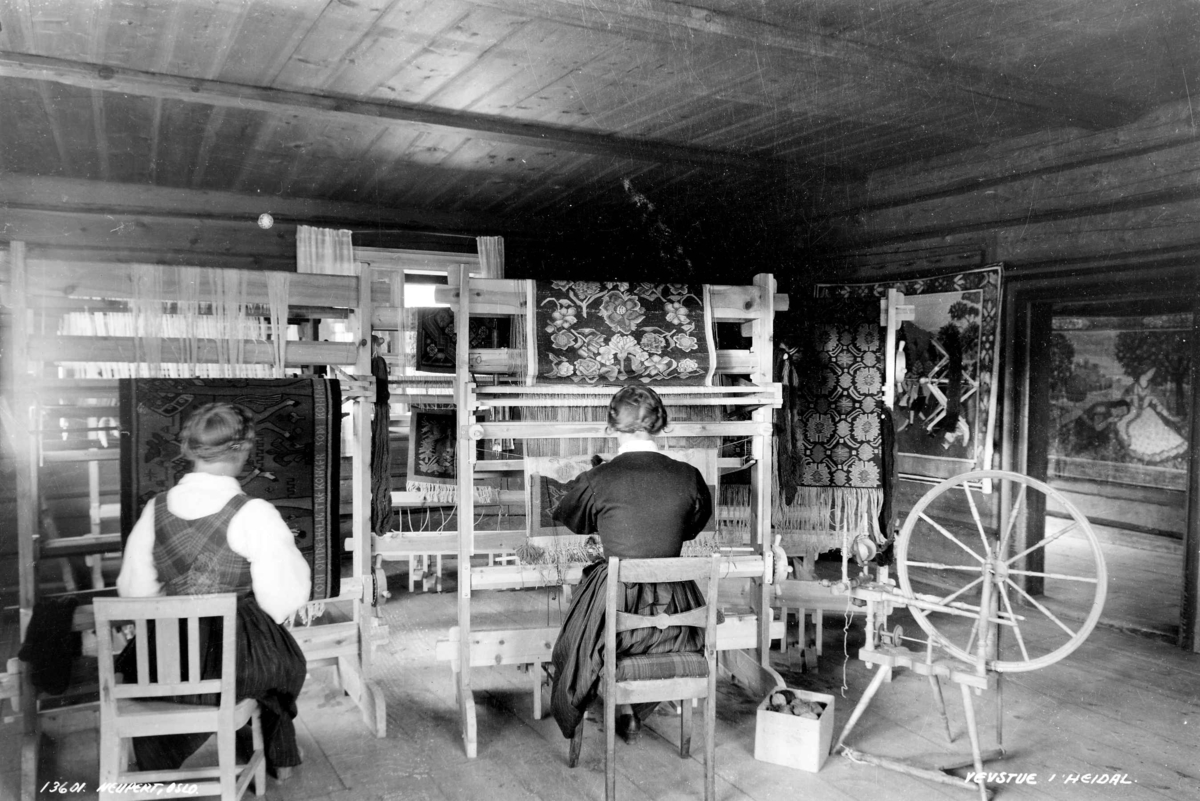 Hermann Christian Neupert, Vevstue med to vevende kvinner. Prestgard, Heidal, Oppland 1935. Vevnader under arbeid. På veggene ferdige tepper. En rokk til høyre i bildet.