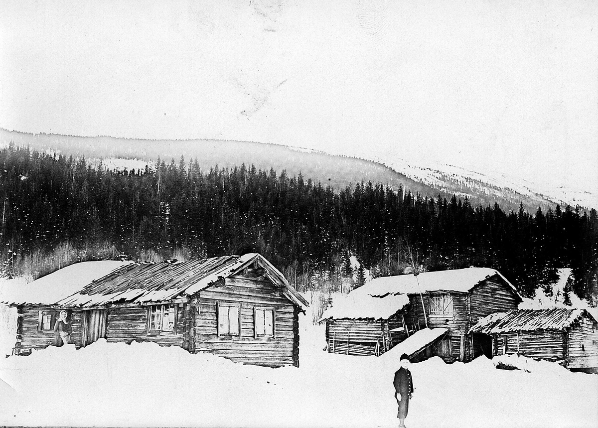 Robert Collett, Gårdsbruk vinterstid med våningshus, låve, stall, ukjent sted. Fjellterreng. Gutt og kvinne utendørs. Serie tatt av Robert Collett (1842-1913), amatørfotograf og professor i zoologi.