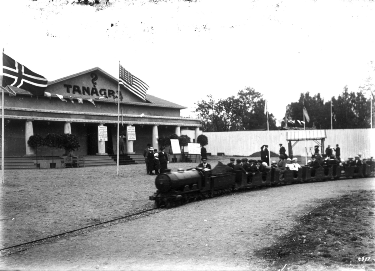 Hermann Christian Neupert, Jubileumsutstillingen på Frogner, Oslo, 1914. Tanagra dukketeater i bakgrunnen. I forgrunnen en lilleputtbane. Tog for publikum. Norsk og amerikansk flagg.
