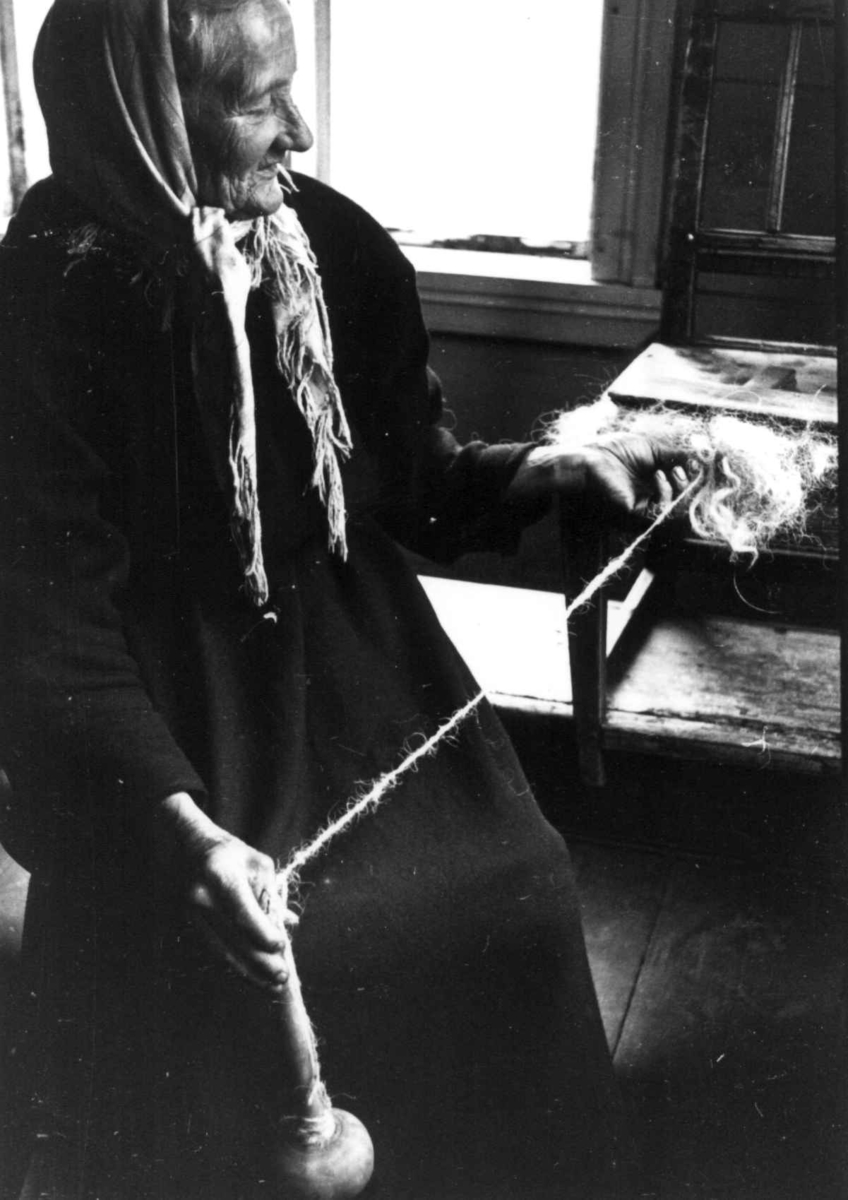 Anna Grostøl, Ragnhild Åvitsland spinner kutagl og grov ull på en liten hjemmelaget håndrokk i tre. Eiken, Hægebostad, Vest-Agder 1941.
