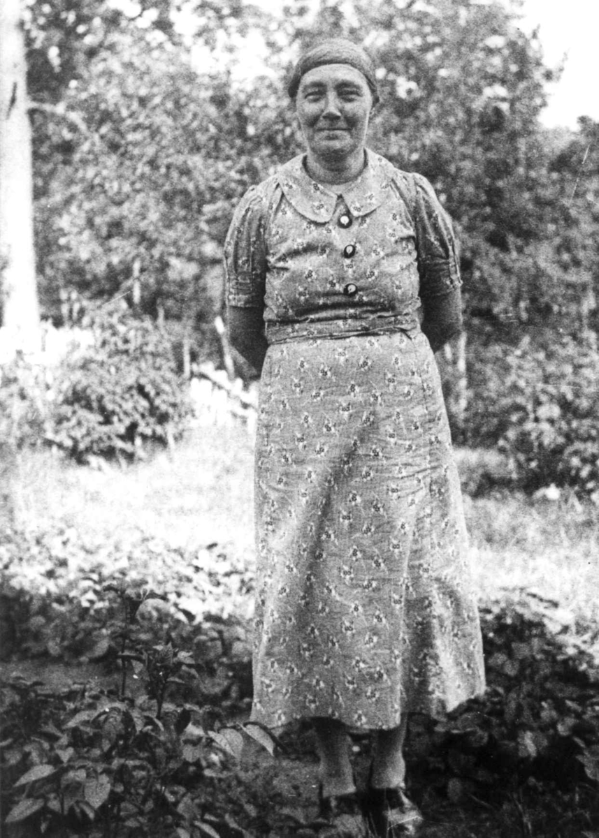 Anna Grostøl, Portrett av en kvinne som står i en hage. Tveit, Kristiansand 1937.