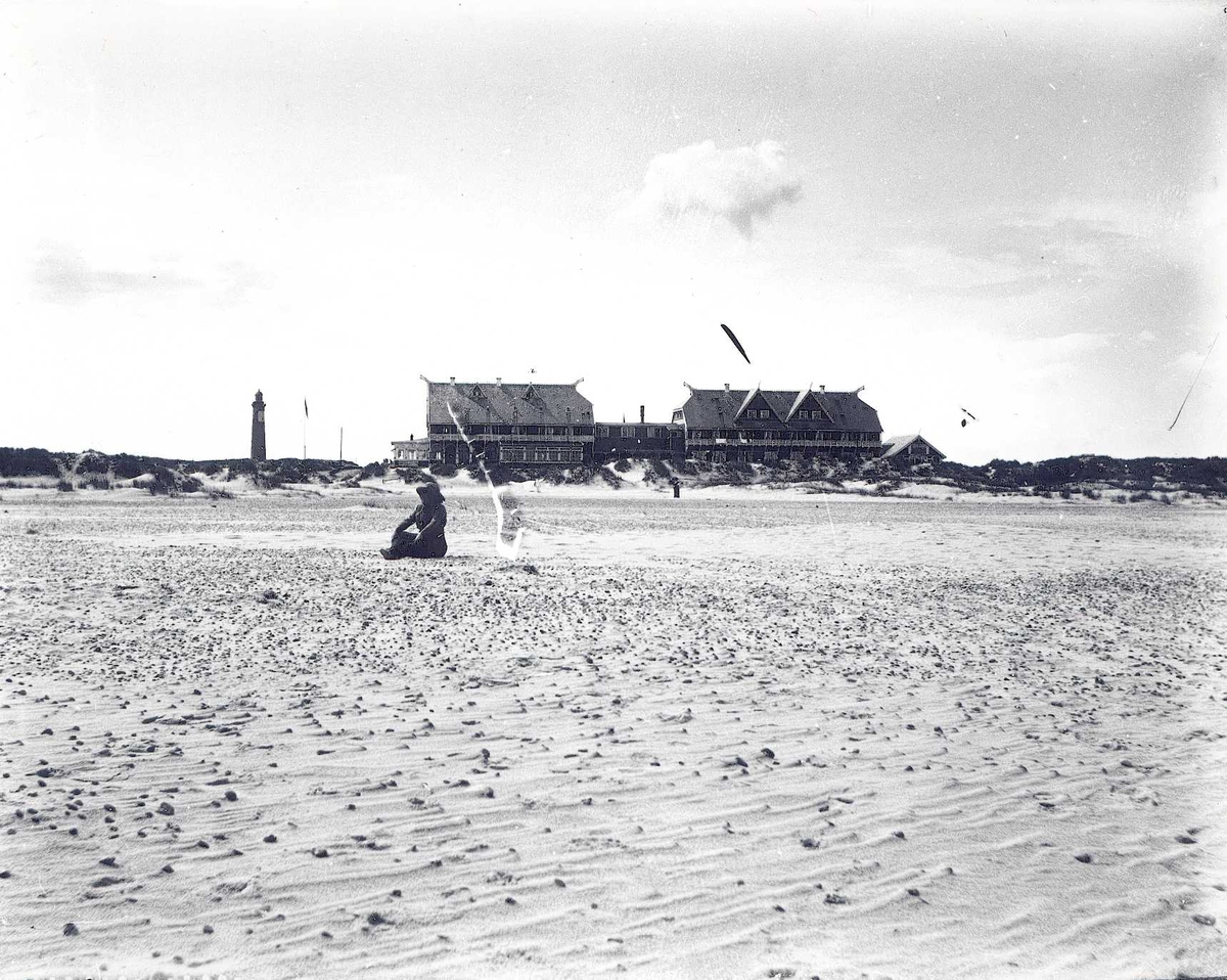 Tom Kent, Strandhotel med dragehoder. Kvinne sitter på stor sandstrand. Fyrlykt i bakgrunnen.