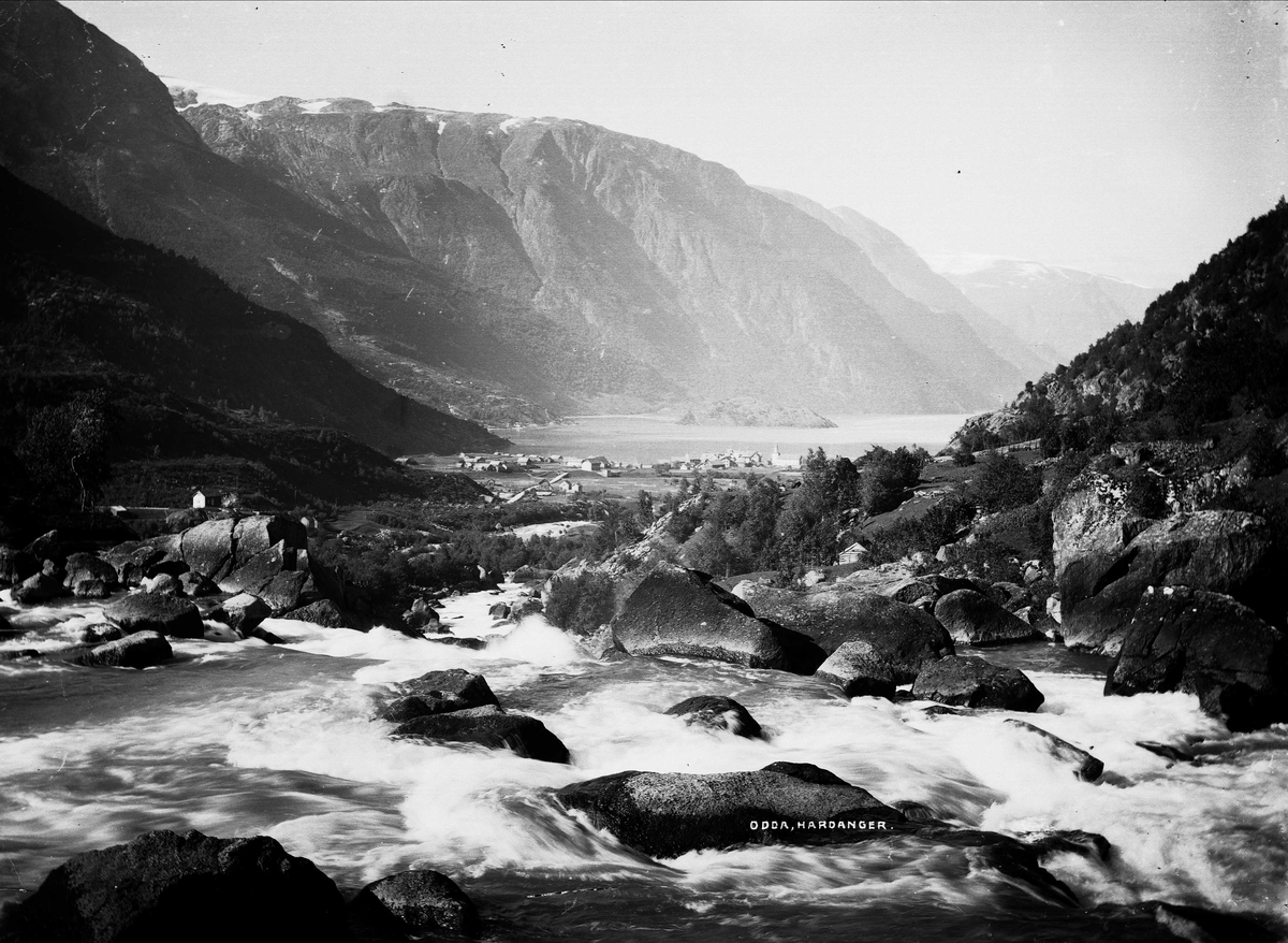 Solveig Lund, Landskapsfotografi fra Odda i Hardanger. I bakgrunnen sees Sørfjorden og i forgrunnen antakelig Opoelva. I midten sees Odda med kirken og Hardanger hotell.