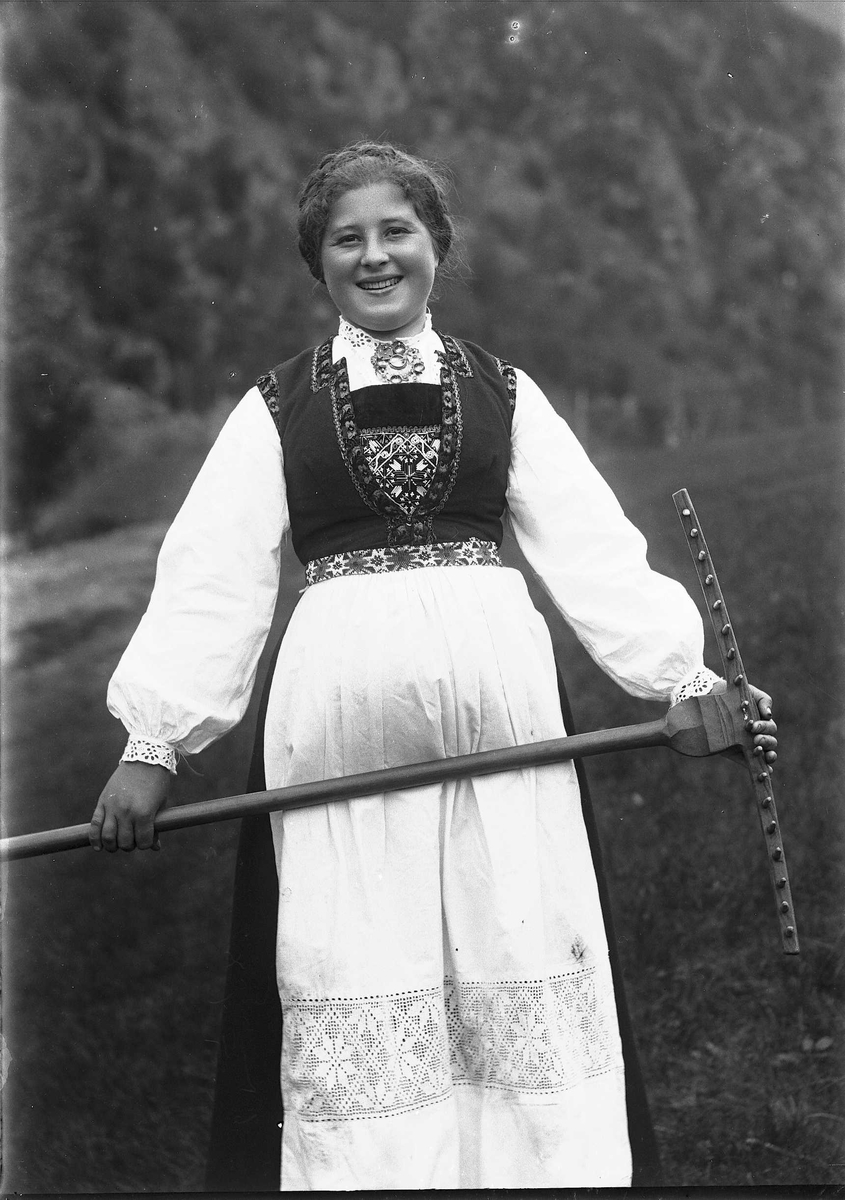 Solveig Lund, Kvinne i drakt stående på jorde med rive i hånden.