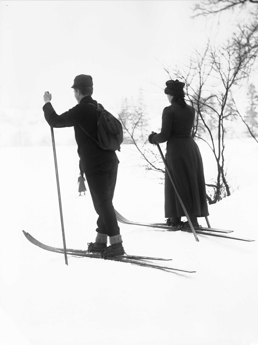 Solveig Lund, Mann og kvinne i snødekt landskap. Fotografert fra siden - begge med ski på beina.