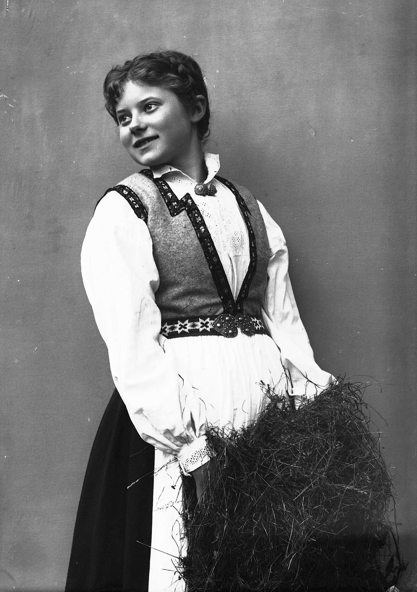 Solveig Lund, 3/4 dels studioportrett av kvinne i drakt og oppsatt hår. Hun holder høy i armene og kikker ut mot venstre i fotografiet. Nøytral bakgrunnen.