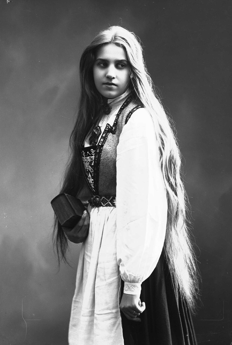 Solveig Lund, 3/4 dels studioportrett av kvinne i drakt med utslått hår. Hun holder en bok i høyre hånd. Bakgrunnen er nøytral.