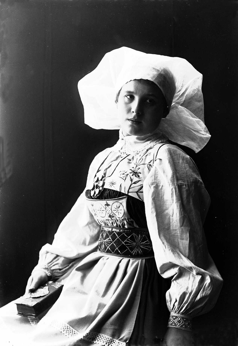 Solveig Lund, Studioportrett av kvinne i drakt og skaut. Hun sitter og holder en bok i høyre hånd. Bakgrunnen er nøytral.