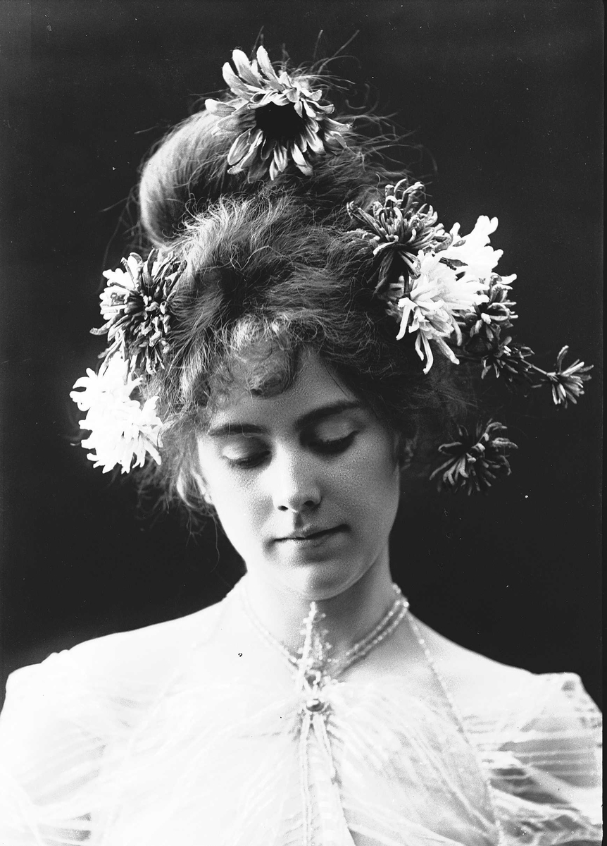 Solveig Lund, Studioportrett av kvinne i kostyme, oppsatt hår og halssmykke - hvit overdel og blomster i håret.