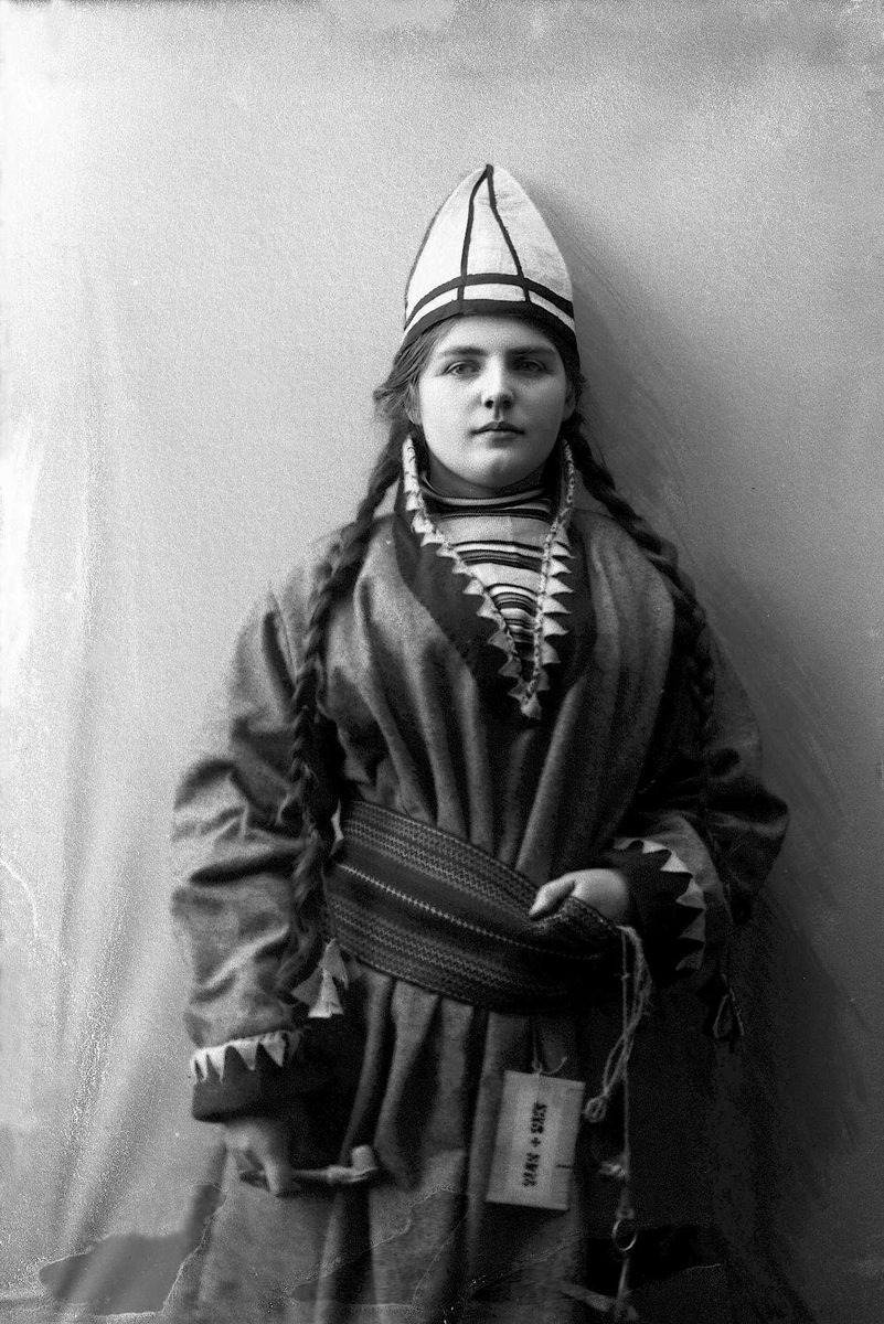 Solveig Lund, Kvinne i samisk drakt - kofte, lue og nålehus med beltering. I den ene hånden holder hun en pipe.