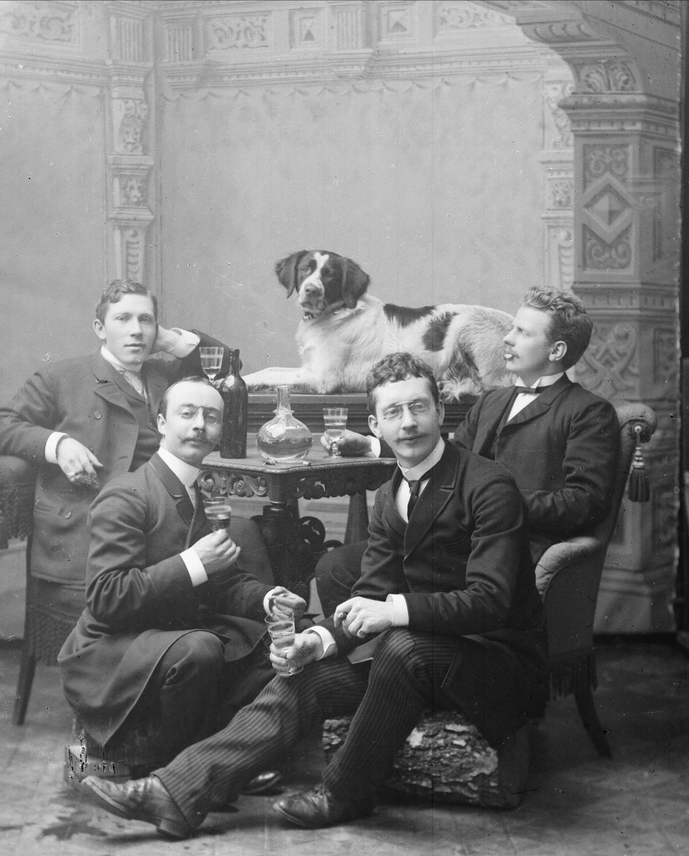 Gustav Borgen, Gruppeportrett, herrer sittende rundt et bord med glass og flasker, en hund i bakgrunnen