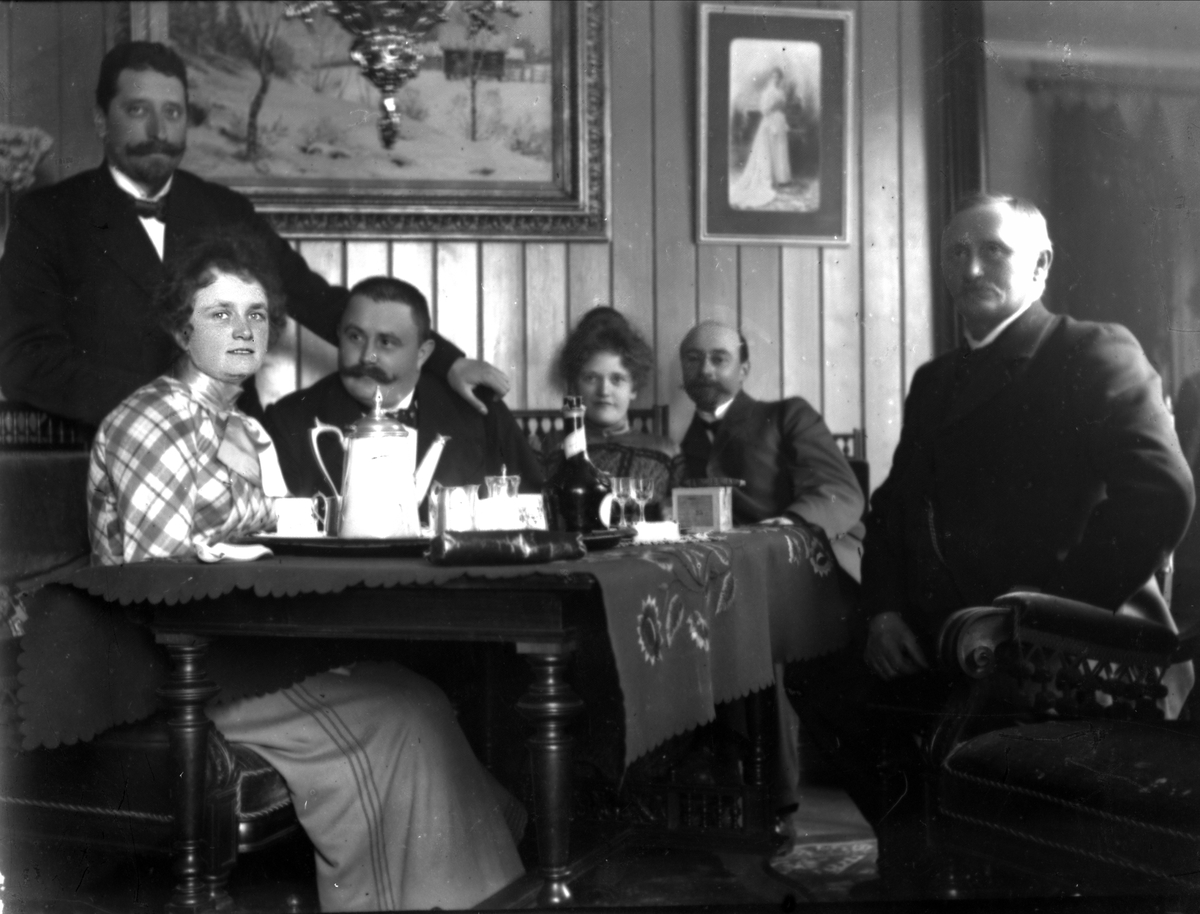 Gustav Borgen, Gruppe mennesker rundt dekket kaffebord i stueinteriør. Avfotografert(?)