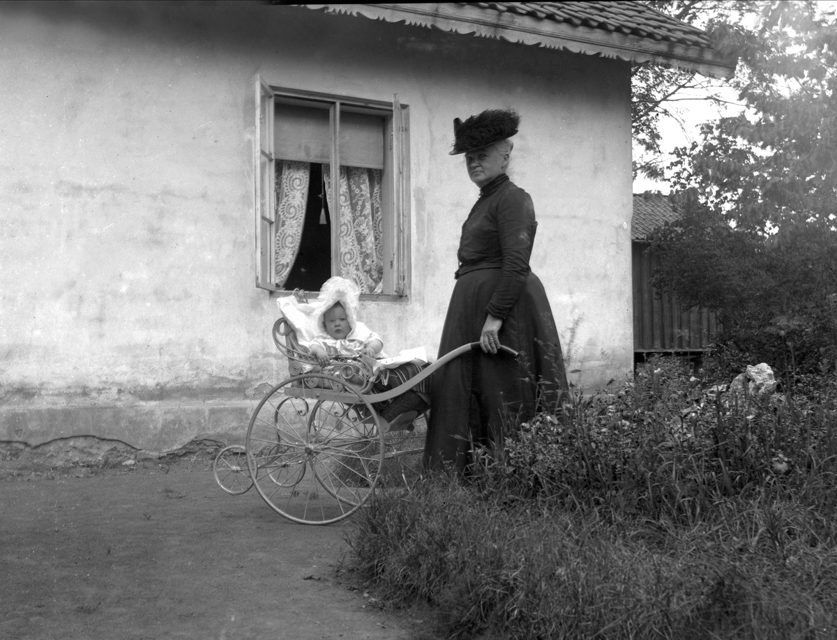 Gustav Borgen, Eldre kvinne med barn i barnevogn, i hage utenfor pusset murhus. Avfotografering(?)