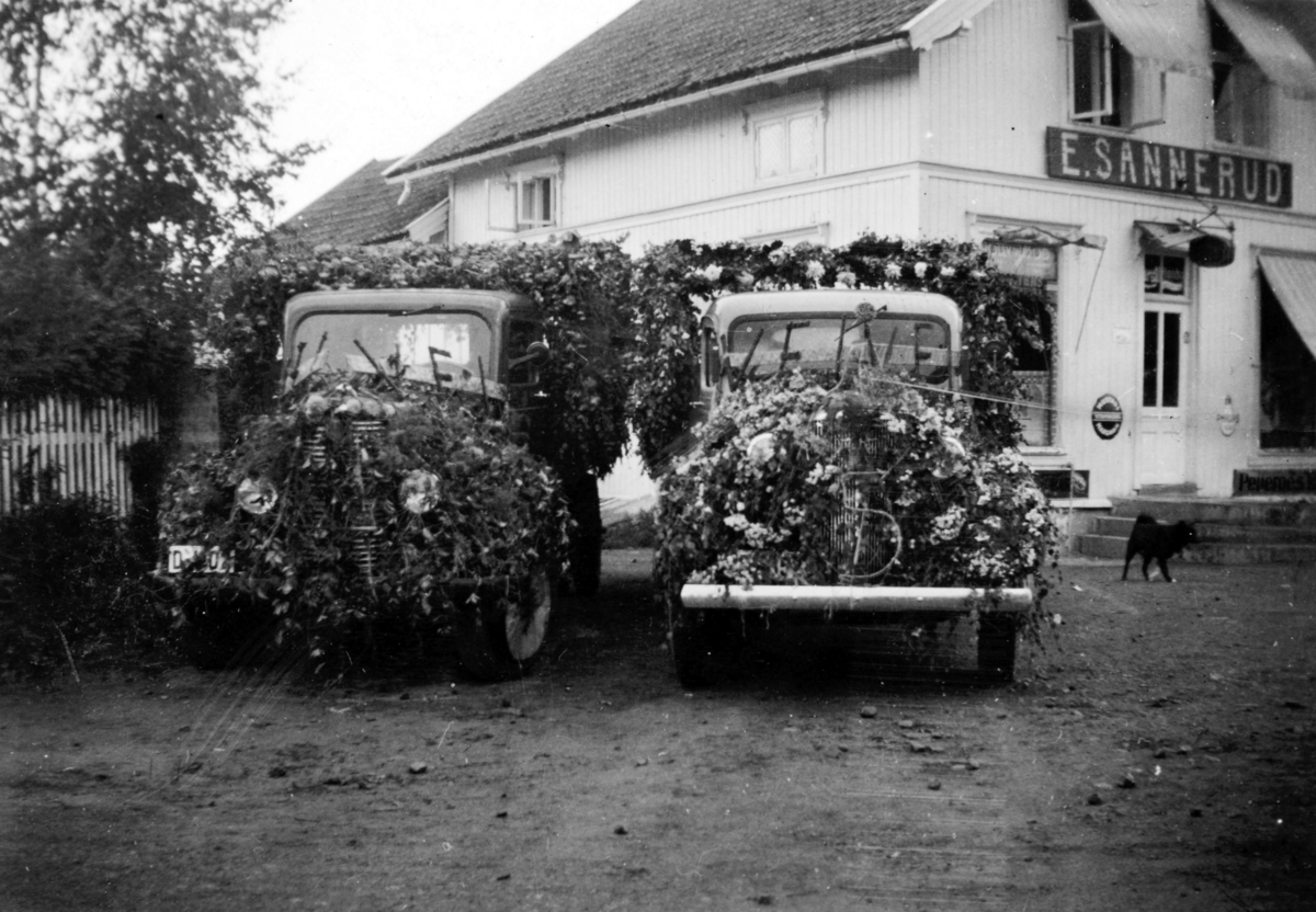 Ukjent, Hamardagen 1938. Lastebiler pyntet med blomster utenfor butikken til E. Sannerud, Vang H.