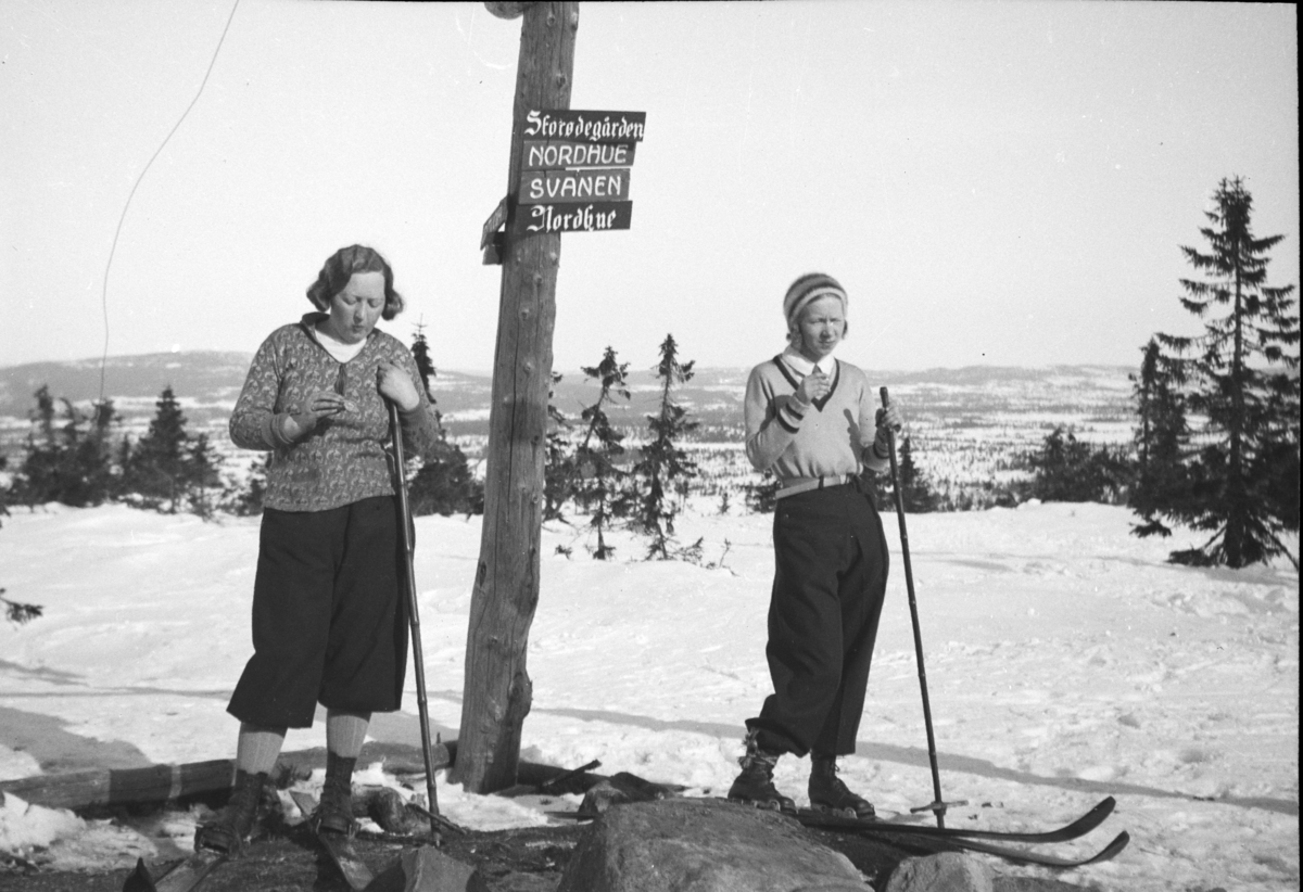 Johs. (Johannes) Johannessen, Vangsåsen, skiløpere, skitur, to kvinner i skiantrekk, løypeskille, skilt. Til høyre står Lumi Johannessen