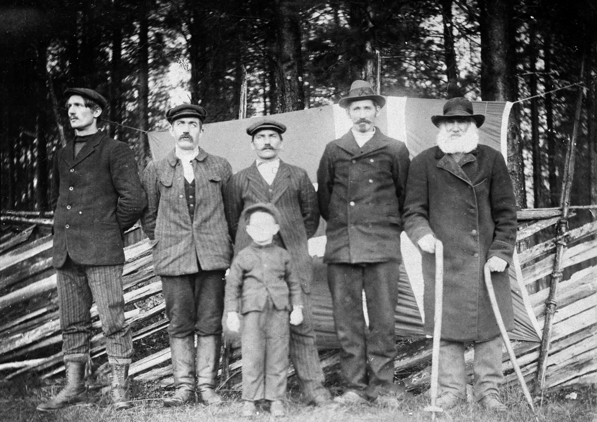 Haakon Garaasen, Gruppe på 5 menn stående foran et gjerde i Støa med et flagg bak seg. En gutt står foran dem. Fra venstre: Petter Opseth (1889 - 1934), Petter Kjellbak (1881), Peter Støa (1873 - 1955), Petter P. Smed (1868 - 1954), Jan Petter Svensen (1823 - 1913). Foran: Petter Persen (Støa) (1908)