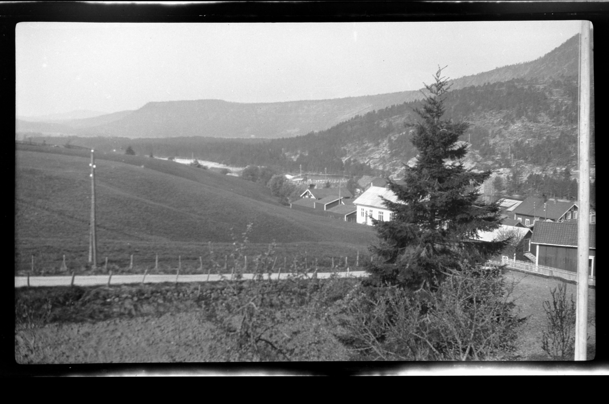 Rolf Sr. Sundt, Ukjent landskap med skogskledd fjell og del av bygd. Fotografert ca. 1928.
