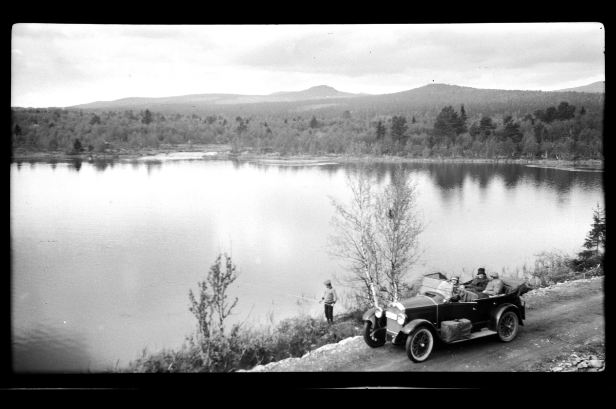 Rolf Sr. Sundt, Hilda Sundt i forsetet, Agnes og Johan Buratti i baksetet på Rolf Sundt Sr.s Buick, en fisker står og fisker i ukjent fjellvann.