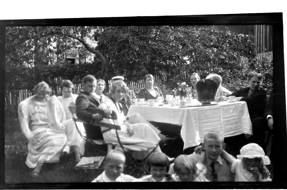 Rolf Sr. Sundt, Voksne og barn samlet til teselskap rundt bord i hage i England. Edna og Percy Stark blant gjestene. Fotografert 1925.