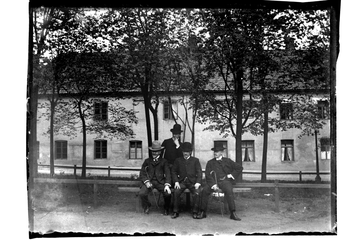Rolf Sr. Sundt, Fire ukjente menn på en benk foran bygård. Fotografert 1903-04.