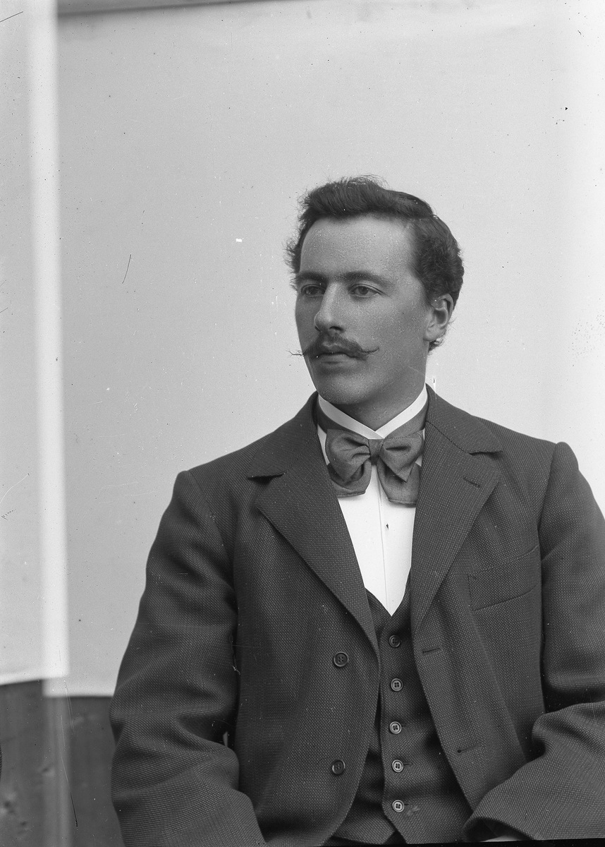 Jakob Jakobsen Engerdal, Ung mann m/bart og mørk dress, sløyfe i halsen, sitter.