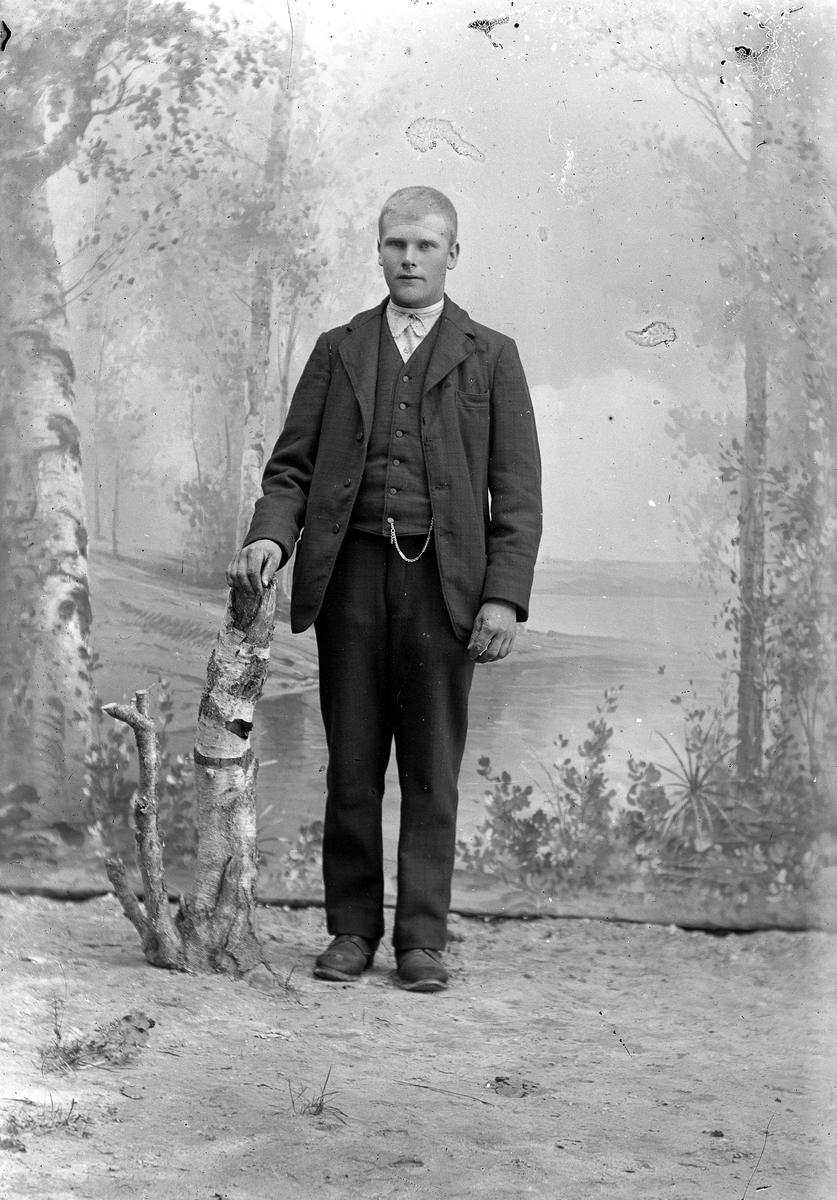 Jakob Jakobsen Engerdal, Ung mann stående ved bjørkestubbe med mørk dress, lys sløyfe og klokkekjede.