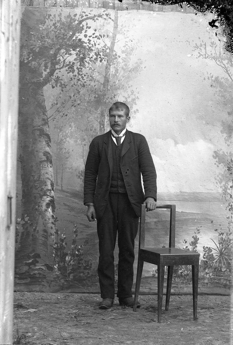 Jakob Jakobsen Engerdal, Ung mann, står ved siden av en stol. Martin Østby(?).