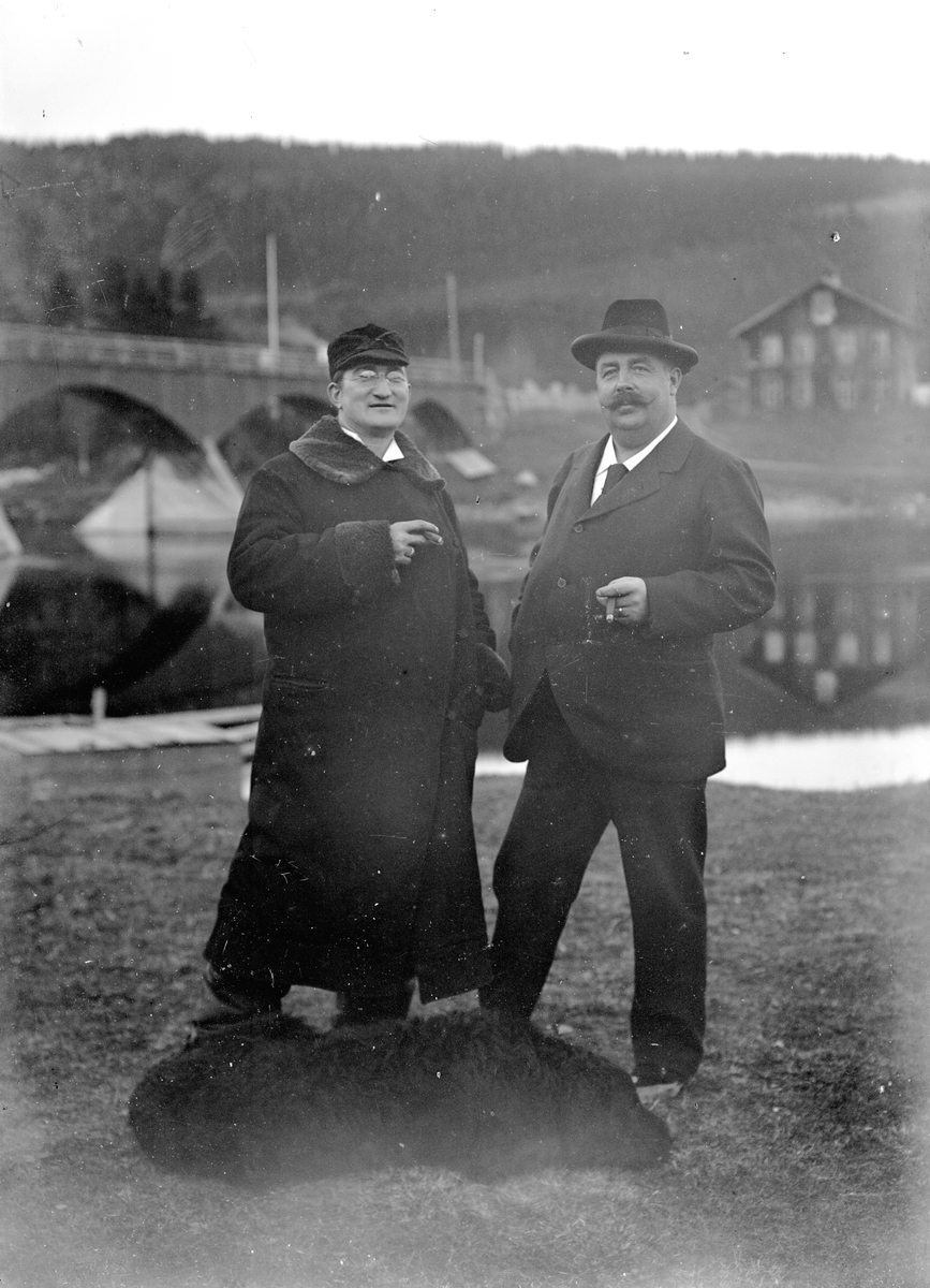 Jakob Jakobsen Engerdal, To menn og en hund foran bru over elva. Til venstre: Doktor (distriktslege i Trysil) Otto Mejlænder (1865-1944).
