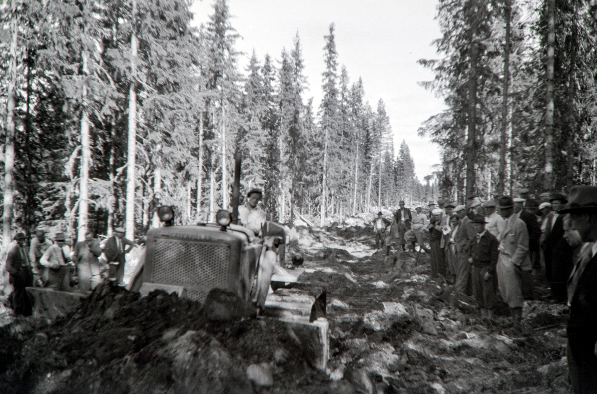 Håkon Prestkværn, Buvika sagbruk, skogbefaring, Ringsaker allmenning. Juni 1949. Gruppe mennesker ser på en bulldozer i arbeid. Bulldozerfører er Sigurd Johan Thomassen f.1925