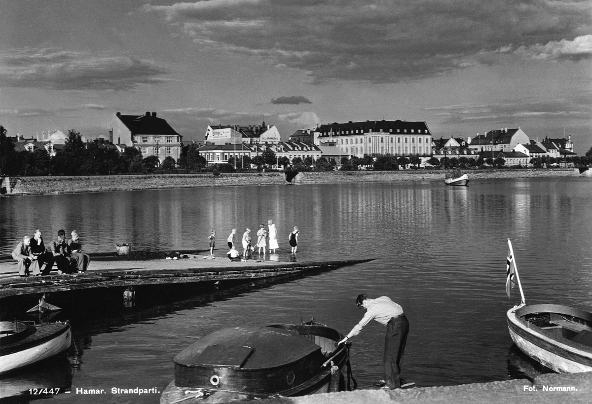 Anno Domkirkeodden, HAMAR BRYGGE, BYPANORAMA, HAMARBUKTA, BÅTER. FOLKELIV PÅ BRYGGA. I BAKGRUNNEN BUNDEFJORD OG BEBYGGELSEN I STRANDGATA. NAVN BÅ BARNA PÅ BRYGGA. FRA VENSTRE PÅ BENKEN: SVERRE AMUNDSEN, REIDAR ØSTBY, BJARNE GULDBRANDSEN, ODD MOEN OG GUNNAR EVENSEN. I VANNKANTEN FRA VENSTRE : IVAR JENSEN, MAGNE EVENSEN…
