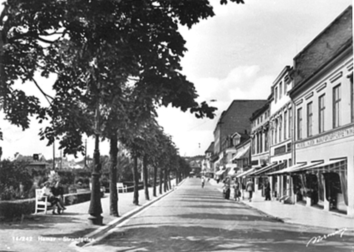 Anno Domkirkeodden, OVERSIKT STRANDGATEHAGEN, STRANDGATA 13 OG 15. FOLK, BENK, TIL HØYRE WIEBERG & hAGEN MANUFAKTURFORRETNING, STØKKEN BOK OG PAPIRHANDEL, E. HAMMERSTAD OPTISKE FORRETNING OG FOTPLEIE.