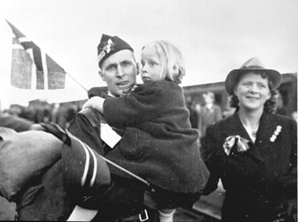 Anno Domkirkeodden, GRINIFANGER KOMMER HJEM, FAR: KRISTIAN B. GUNDERSEN MED DATTER INGER SYNNØVE PÅ ARMEN, TIL HØYRE: SYNNØVE GUNDERSEN, HAMAR JERNBANESTASJON, FRIGJØRINGSDAGENE 1945. GUNDERSEN BLE SENERE VARAORDFØRER OG ORDFØRER I HAMAR.
