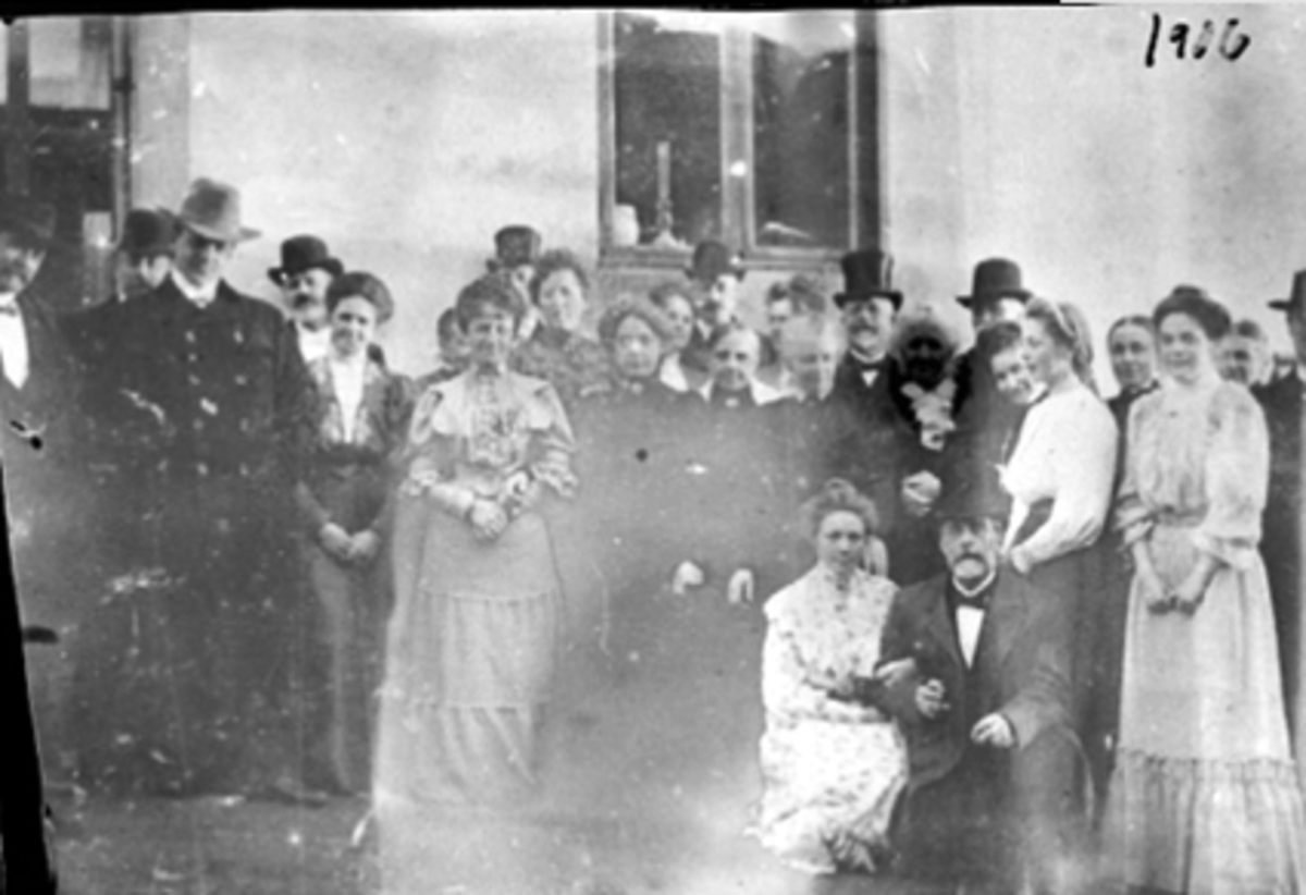 Anno Domkirkeodden, STOR GRUPPE FESTKLEDDE MENN OG DAMER FORAN HUS, SKOLEGATA 12