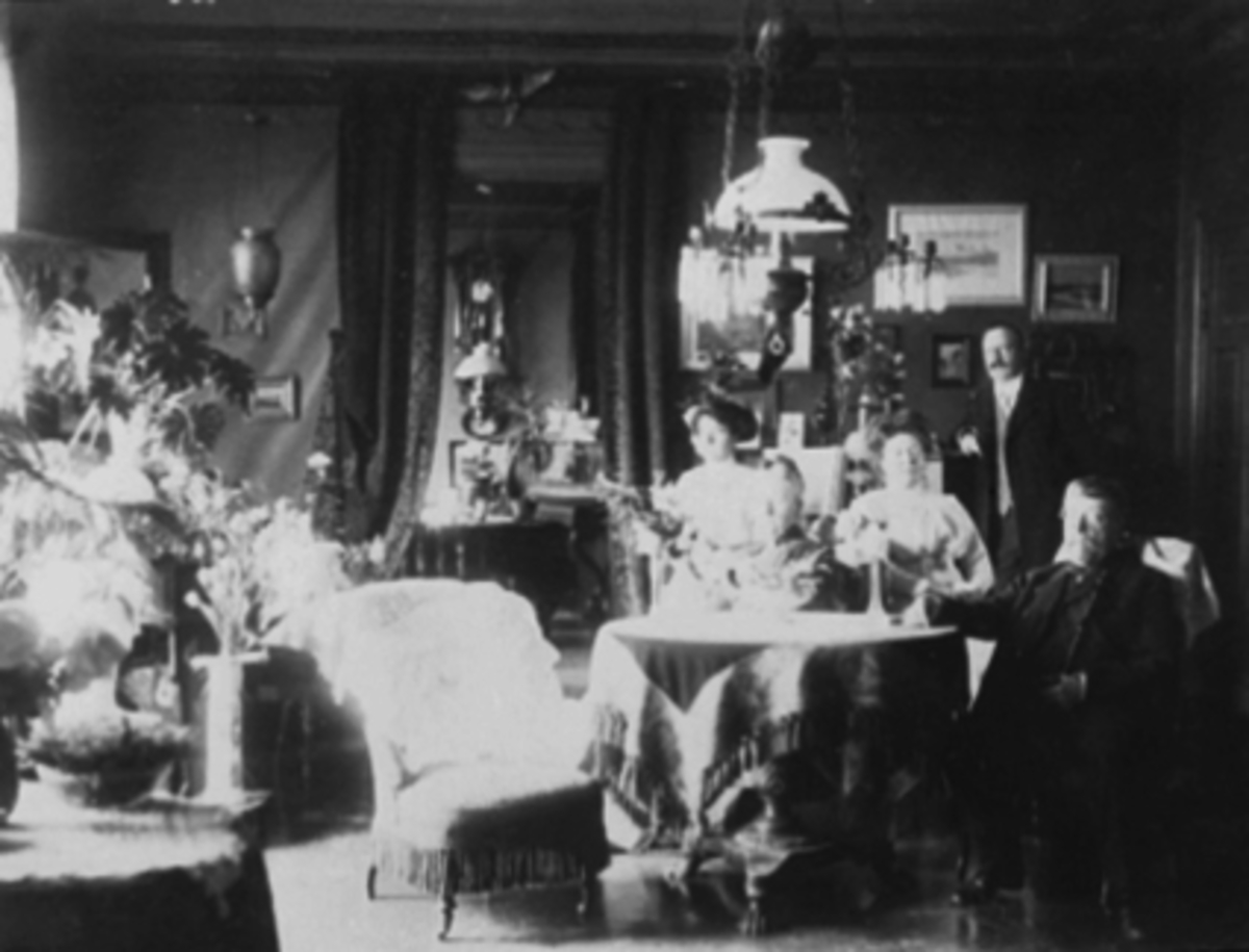 Anno Domkirkeodden, Interiør, sorenskriverfamilien Piro, gruppe 5 personer. Eldste datter Marie Piro f. 1868, yngste datter Anne Cathrineeldste sønn Kristian Piro, Andreas Christian Jachim Dorp Piro, og hans søster fru Henschien. Veggur og bord befinner seg hos bildets eier.