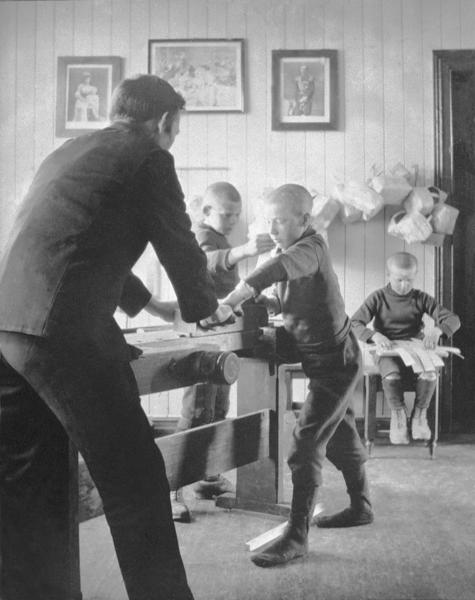 Anno Domkirkeodden, Interiør fra arbeidsrom på Toftes Gave, Nedre Sund, Helgøya. Gutt og lærer høvler spon. Gutter fletter kurver.