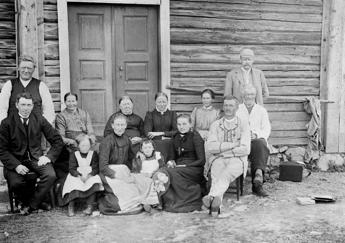 Anno Domkirkeodden, Familien i Nerlien, Nes, Hedmark samlet foran huset. 13 voksne og barn. Fotografens utstyr til høyre.