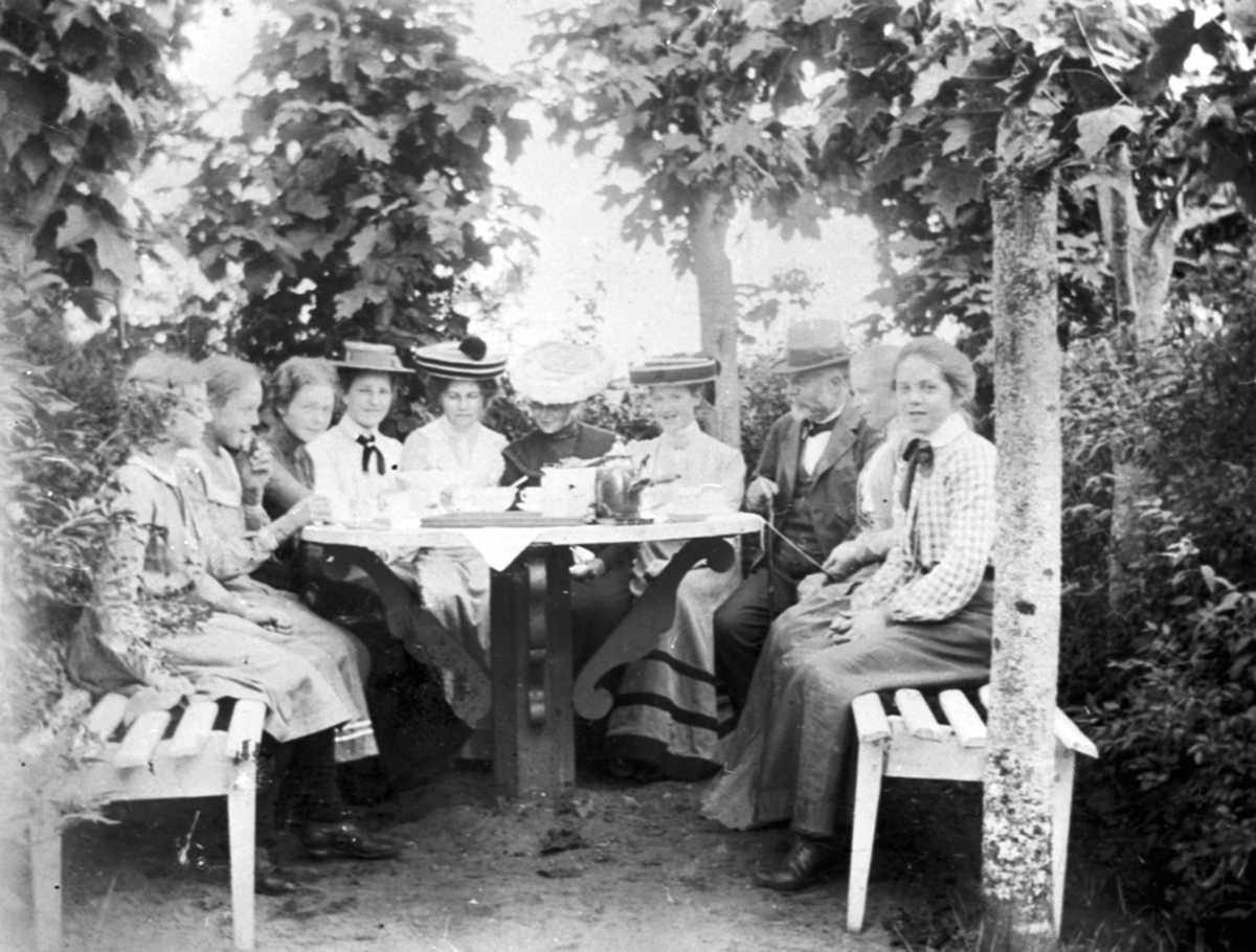 Anno Domkirkeodden, Gruppe damer og en mann rundt et kaffebord i hagen på Vesle-Ile, Furnes, Ringsaker.