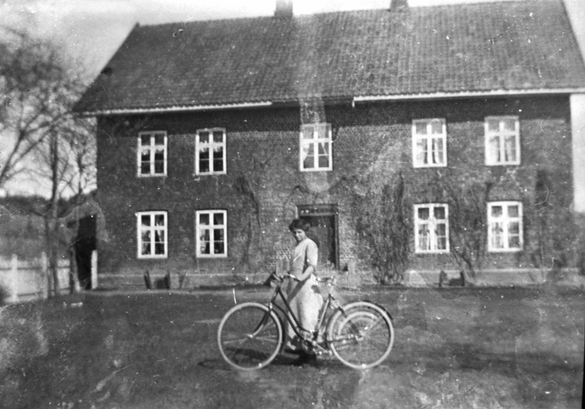 Anno Domkirkeodden, Husjomfru Anne Dystvoll med sykkel utenfor hovedbygningen på Mellom-Kise, Nes, Hedmark.