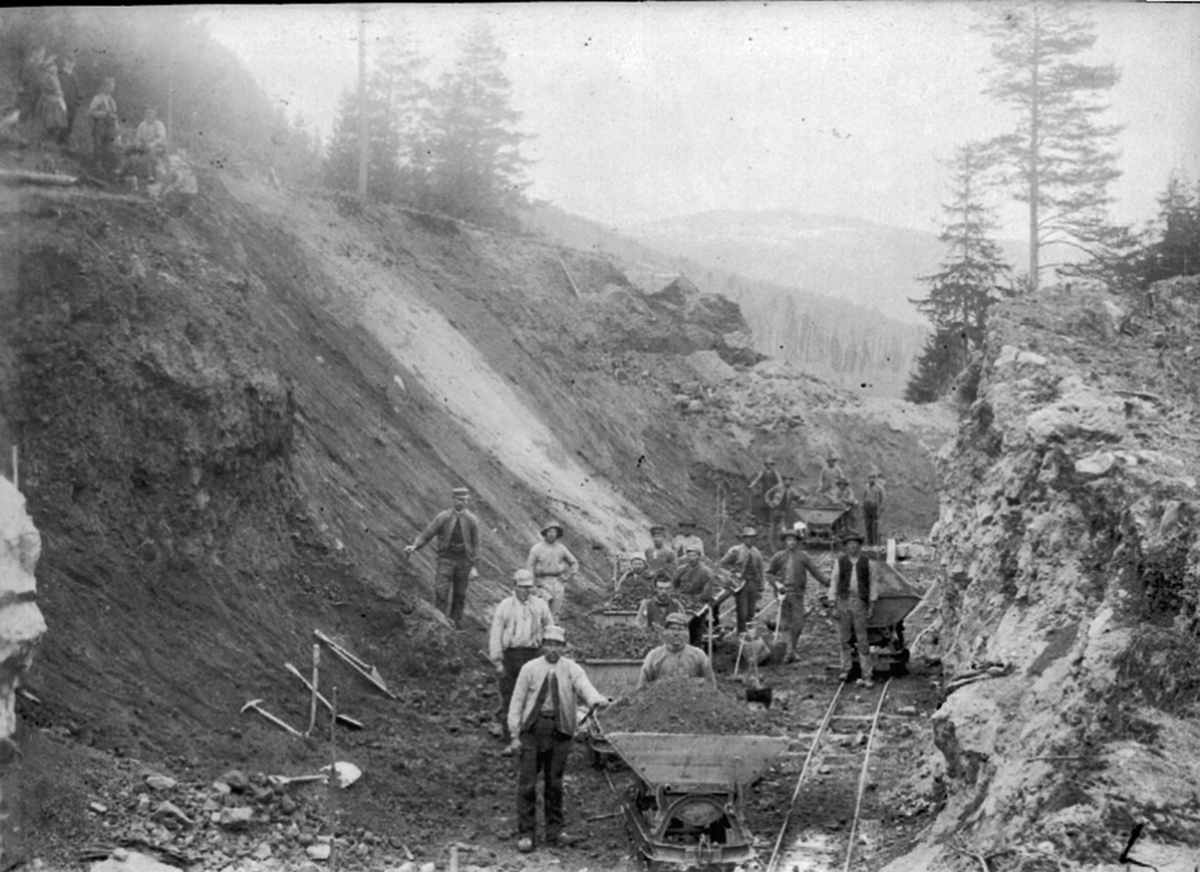 Anno Domkirkeodden, Jernbaneutbygging. Anleggsarbeid, skjæring nedenfor gården Berg, Brøttum, Ringsaker. Arbeidere transporterer jordmasser med vogner på skinner.
