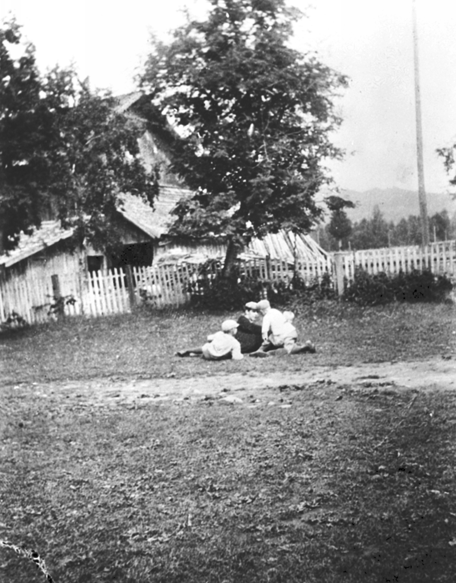 Anno Domkirkeodden, Mann og tre barn i gresset på tunet på Granerud gård, Brumunddal. Våningshus i bakgrunn.