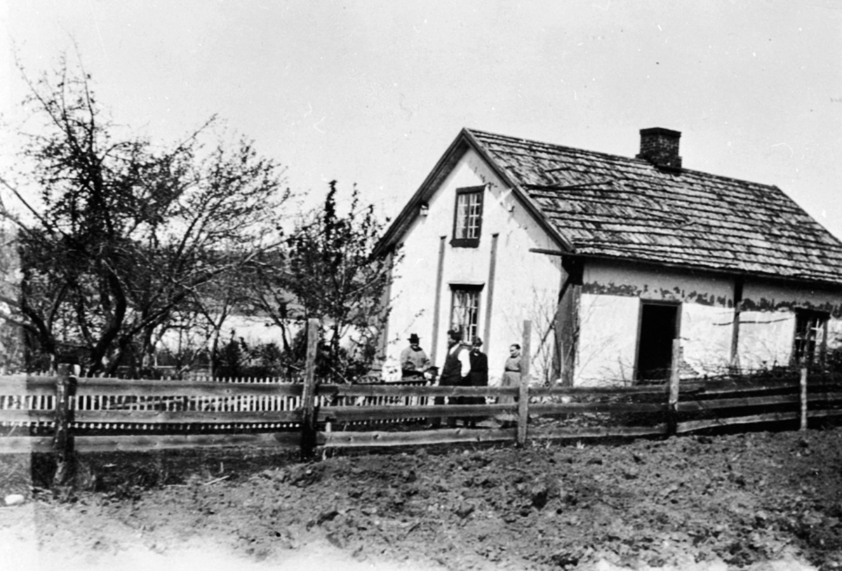 Anno Domkirkeodden, Huset i Sundby lille, Skredderbakken, Helgøya med fruktrær. Utenfor står til venstre Johannes Akselsen og til høyre Marit Jensdatter.