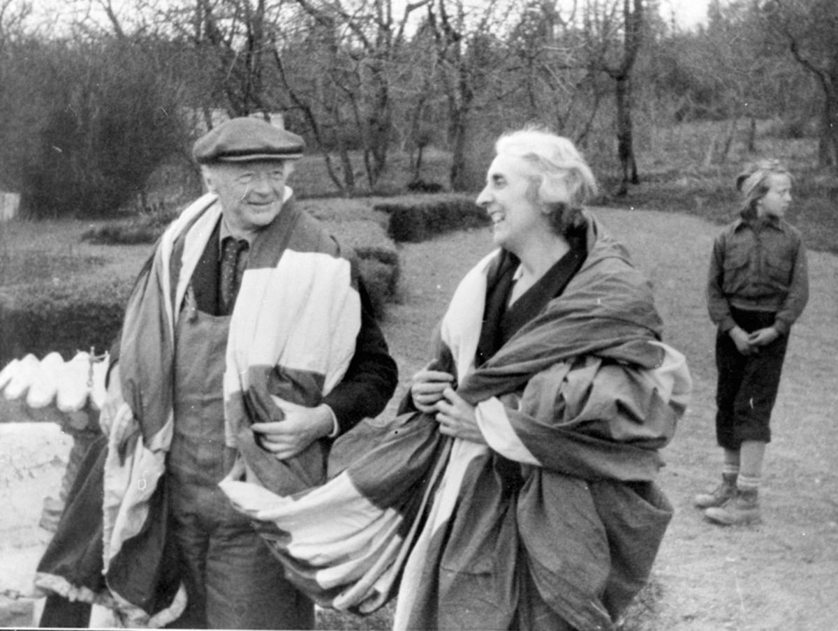 Anno Domkirkeodden, Domprost Reidar Kobro og bispinne Julie Krohn-Hansen med det norske flagg over skuldrene på Hovelsrud, Helgøya i fredsdagene i mai 1945. Nora Johanne Hagen f. 1933 (gift Rise) i bakgrunnen.