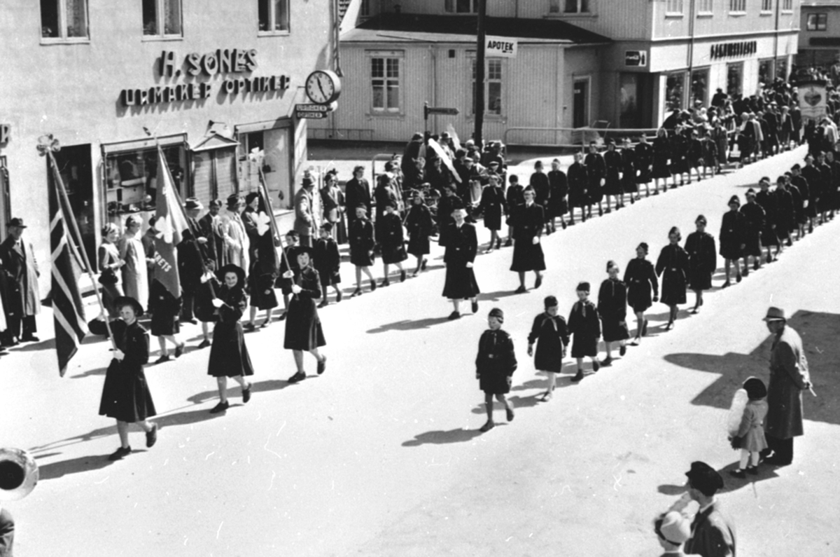 Anno Domkirkeodden, 17. mai. Speidertog med fane foran urmaker Sønes, Furnesvegen, Brumunddal.