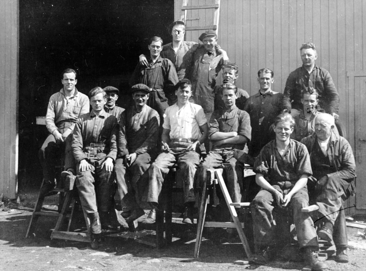 Anno Domkirkeodden, Gruppe arbeidere oppstillt utendørs ved Hymas A/S, Brumunddal Mekaniske Verksted og Støperi. Nr. 2 fra høyre i bakre rekke: Johannes Løvberg f. 15.03.1901 i Furnes. Andreas Hansen, Joh. Tollefsen, Ludvig Andersen, Ludvig Lassesen, Kristian Lilleøen, Sverre Larsen, Bekkevold, er noen av de øvrige pe…