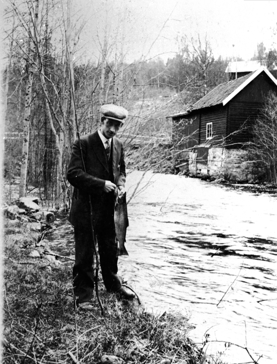 Anno Domkirkeodden, Simen Baardseth med fisk tatt i Moelva, turbinhuset til Moelven Brug i bakgrunnen.